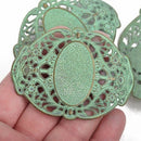 Two large bronze filigree cuff bracelet connectors with a green verdigris patina, displayed in a hand.