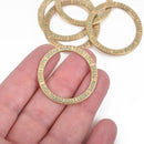 Five light gold affirmation rings with green verdigris patina, held in a hand, with the inscription 'DREAM HOPE TRUST LOVE' stamped on one side.