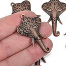 A hand holding a copper elephant pendant charm with detailed metalwork, resembling a Hindu Ganesha elephant head.